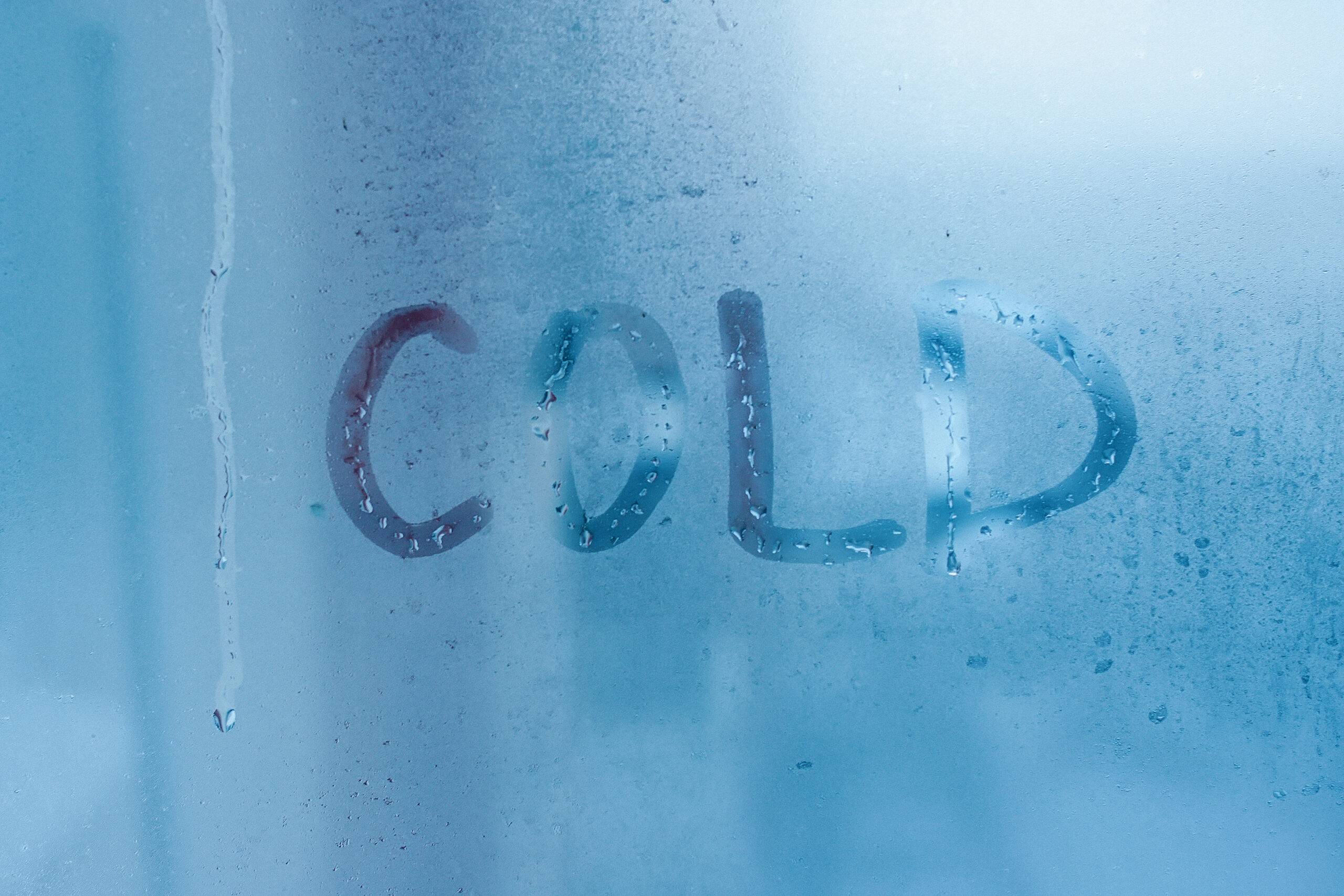 the word cold rubbed onto a frosted piece of glass with someones fingers